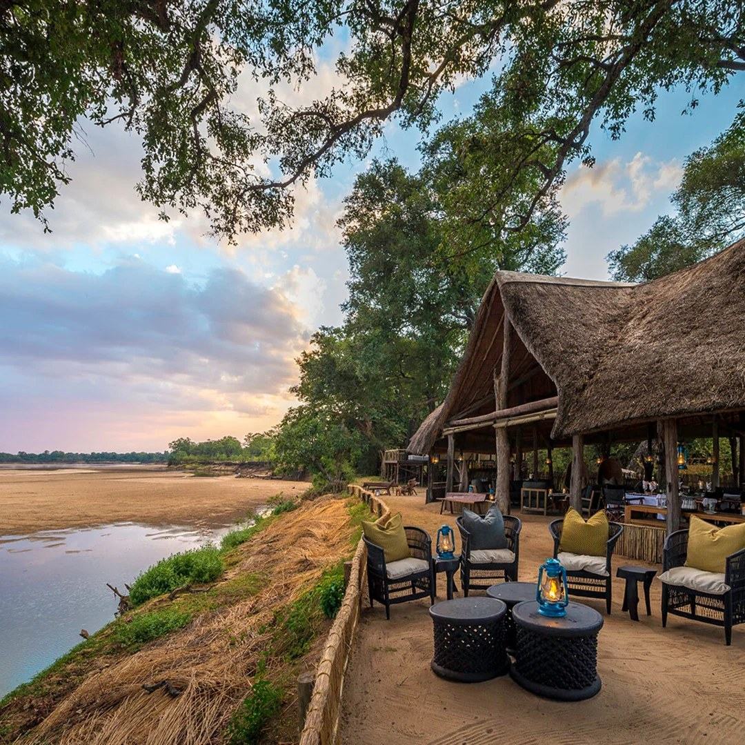 Une terrasse de salle à manger en chaume surplombe le fleuve Luangwa au crépuscule à Chamilandu Bushcamp, South Luangwa