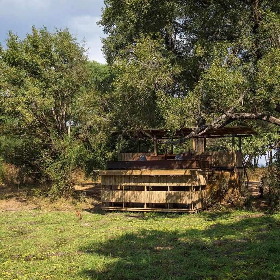 Un affût aux murs de roseaux se dresse sous les arbres près de Chamilandu Bushcamp