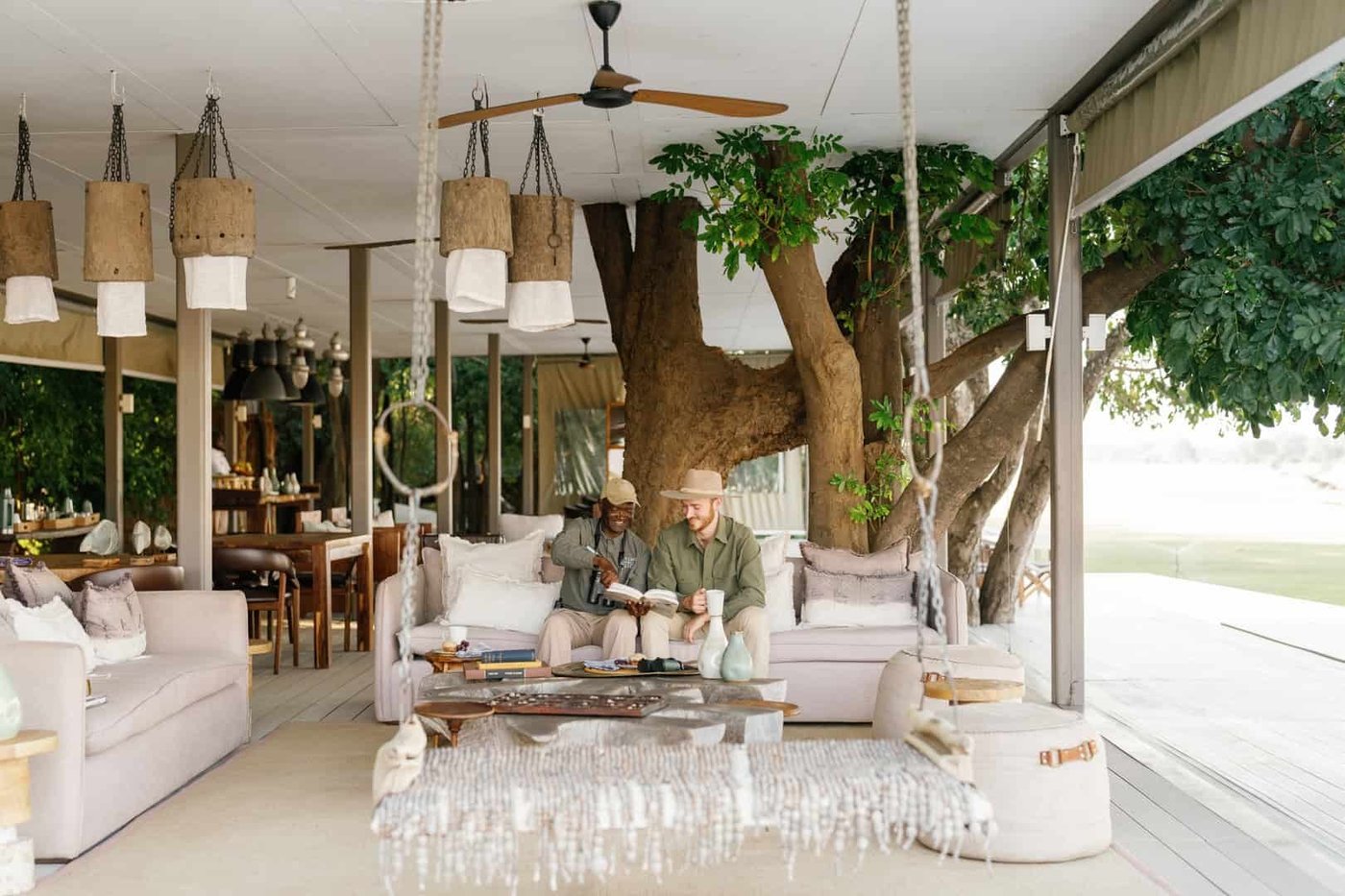 Lounge ouvert avec des chaises en osier suspendues sous un grand arbre à Chinzombo