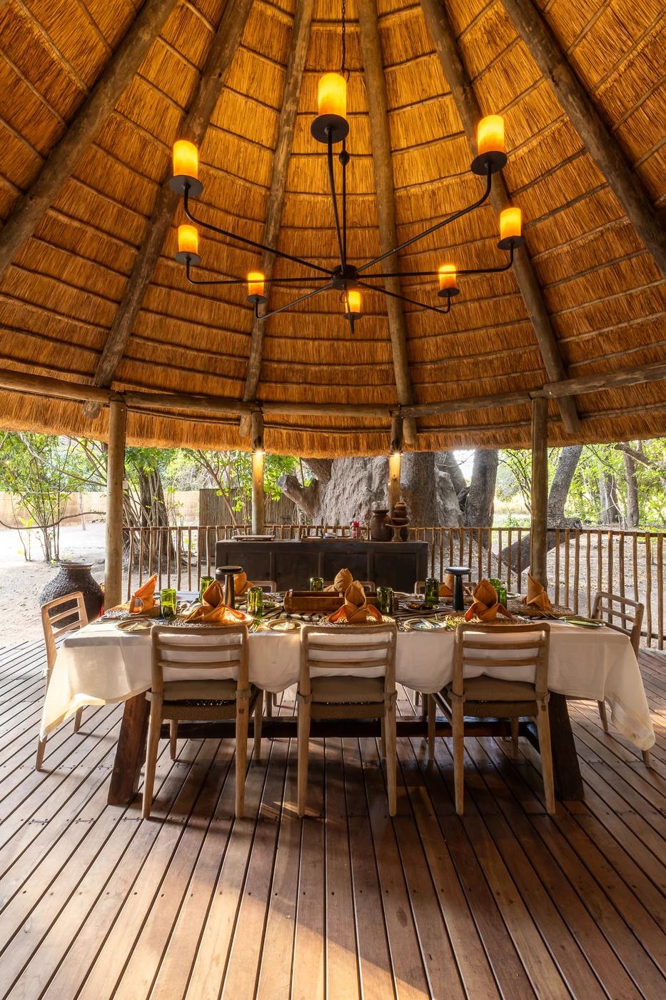Longue table de salle à manger dressée sous un haut toit en chaume à Kuyenda Bushcamp