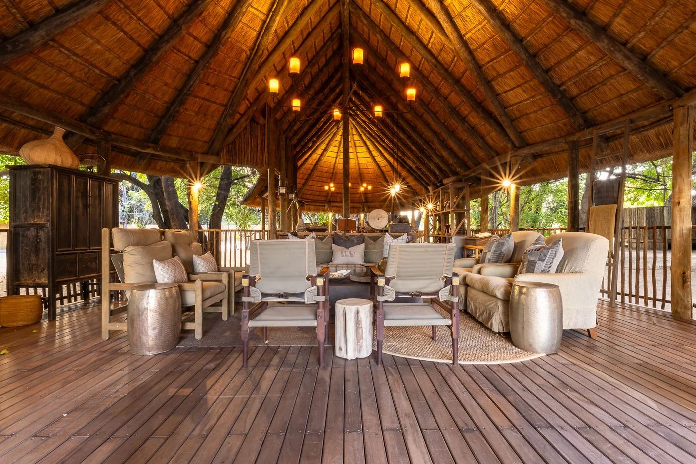 Salon ouvert avec des fauteuils en tissage et des canapés sur la terrasse en bois à Kuyenda Bushcamp