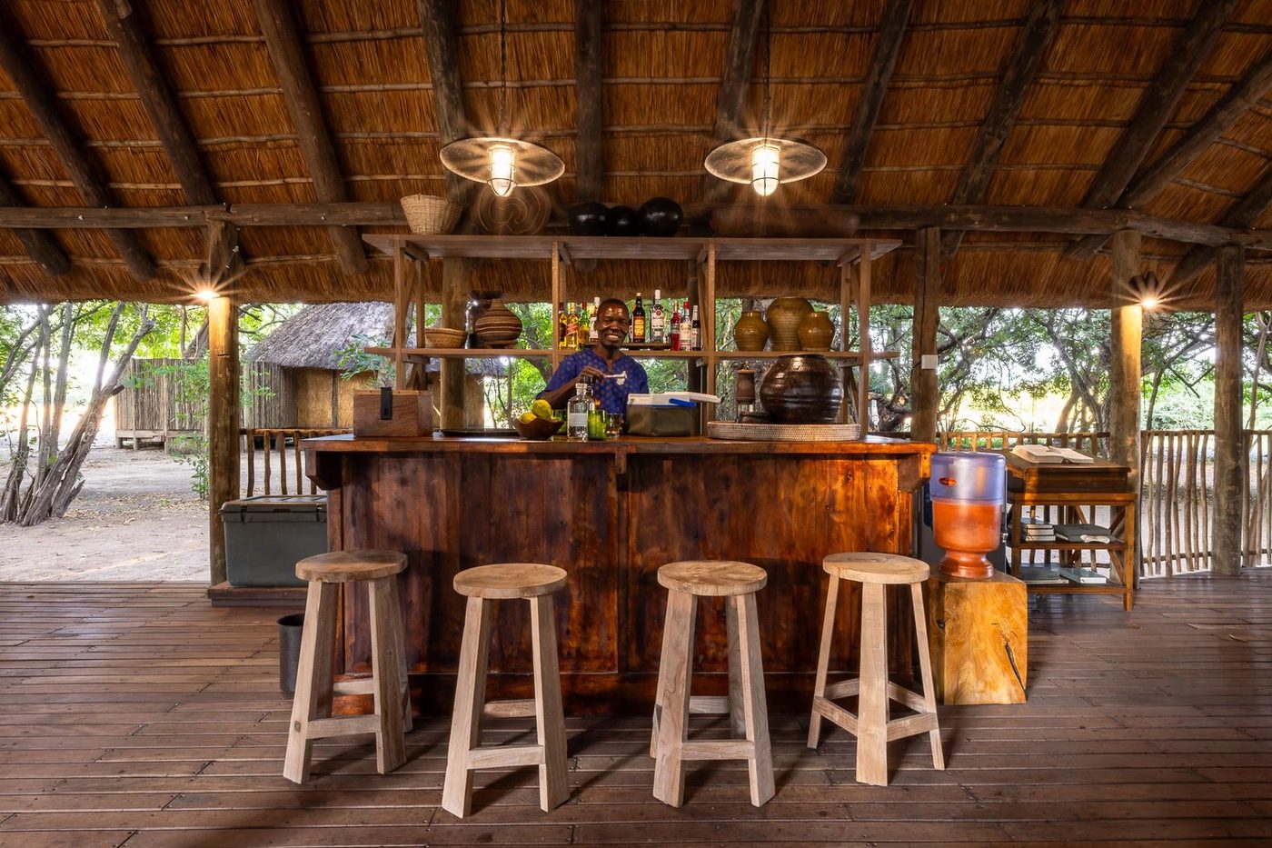 Des tabourets bordent un bar rustique en bois garni de lumières chaudes à Kuyenda Bushcamp