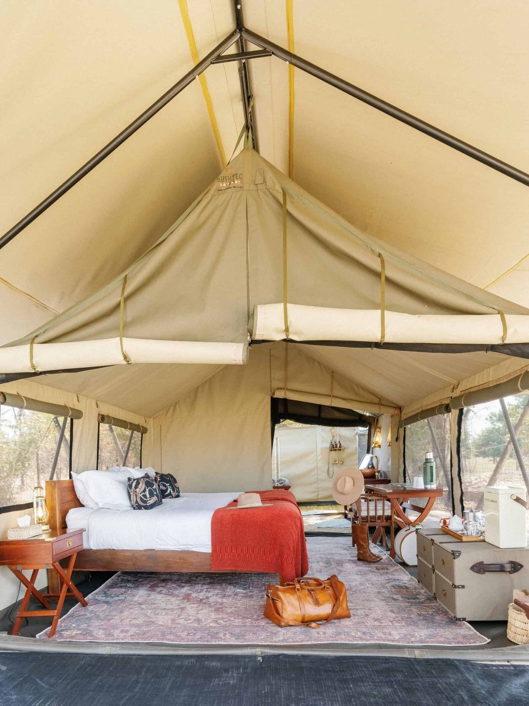 Chambre de tente de safari en toile avec une couverture rouge et un sac en cuir à Luwi