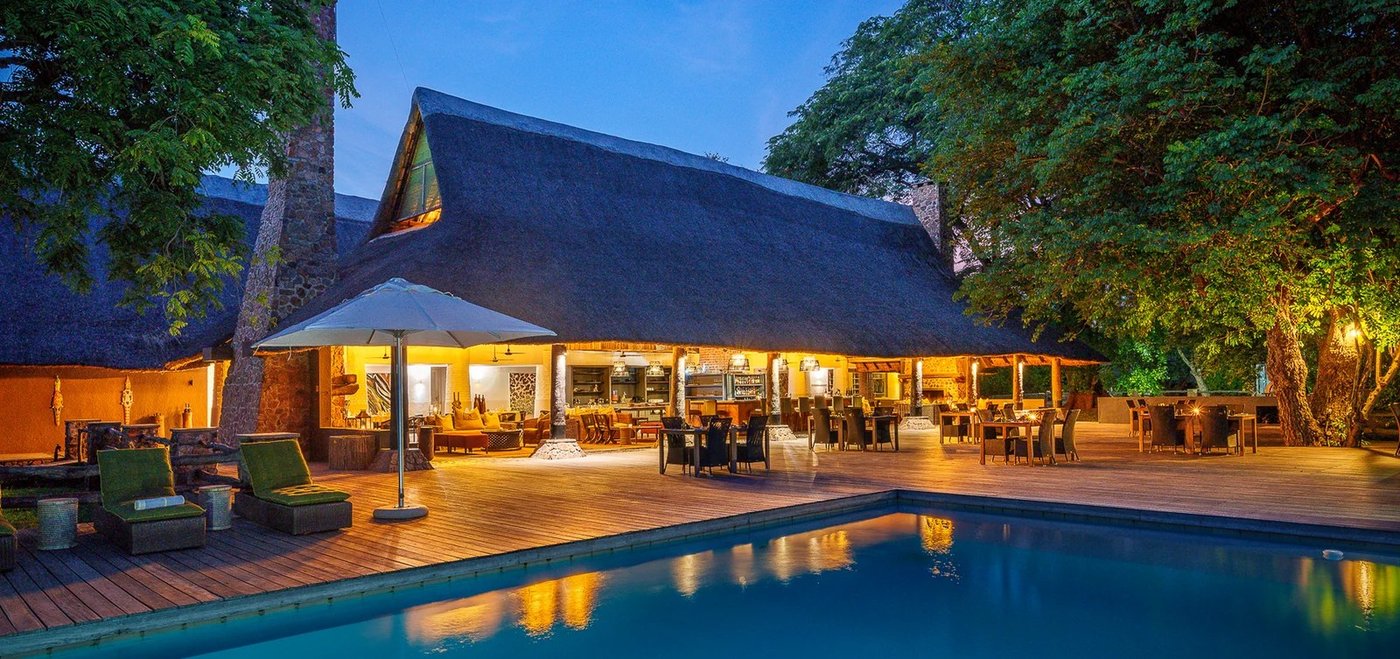 Lodge principal avec chaume et terrasse de piscine illuminées au crépuscule avec tables de restauration en plein air, Mfuwe Lodge