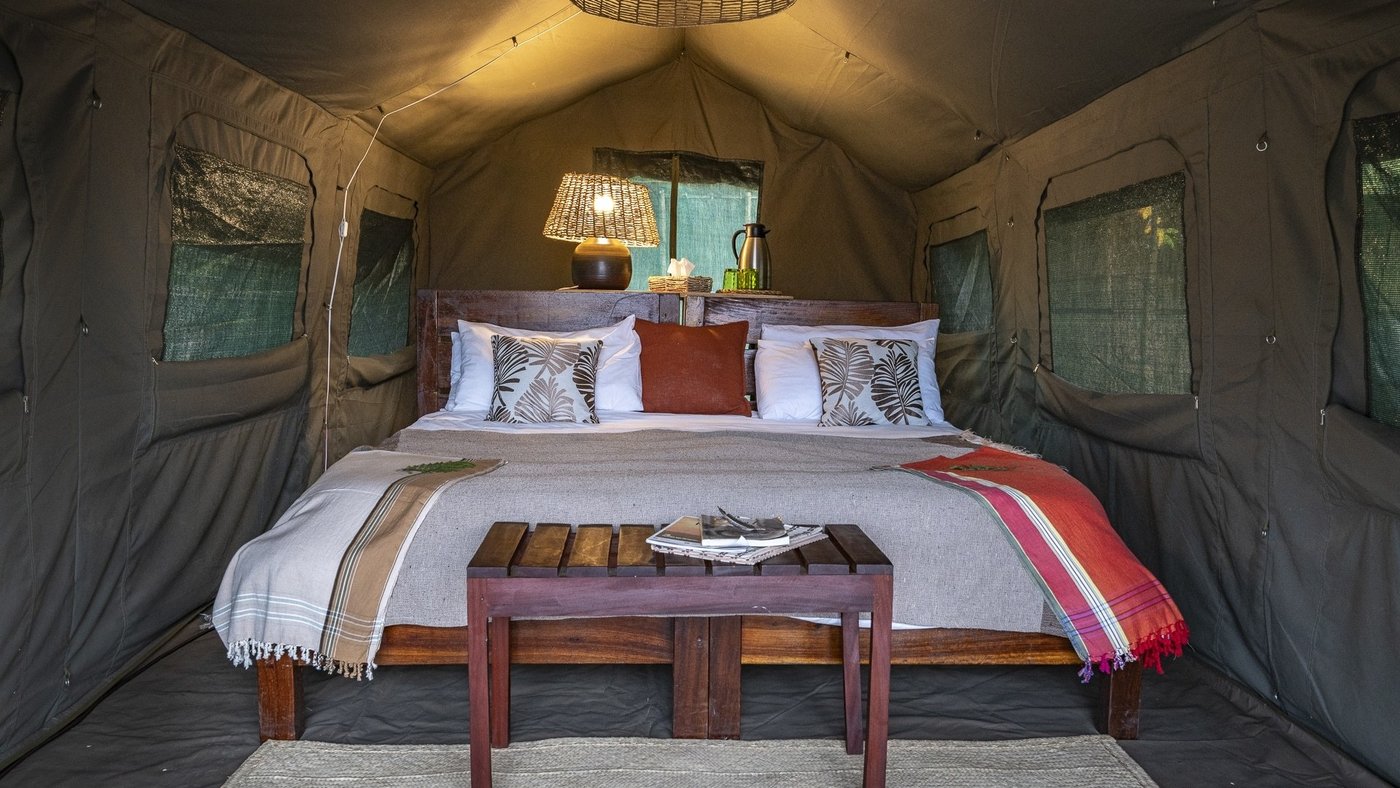 Chambre de tente avec un jeté coloré et une lampe de chevet chez Nkonzi Camp