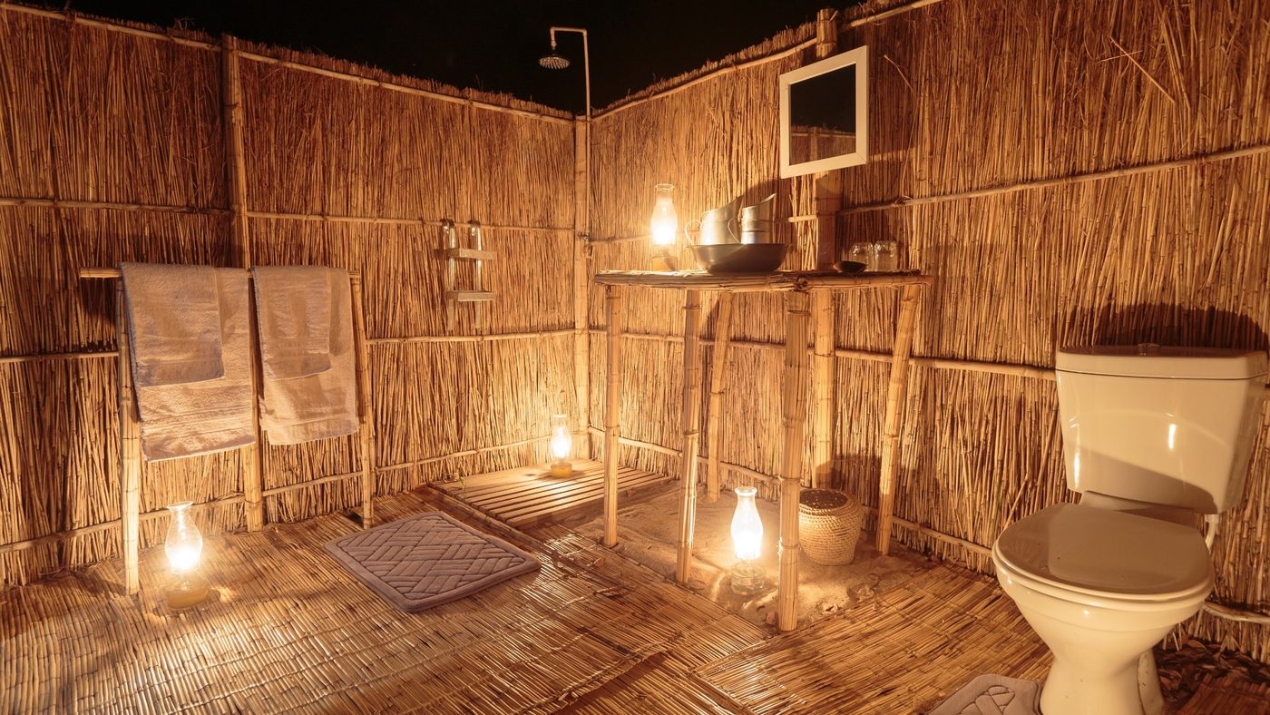 Salle de bain en plein air aux murs en roseaux éclairée à la bougie la nuit, Nkonzi Camp