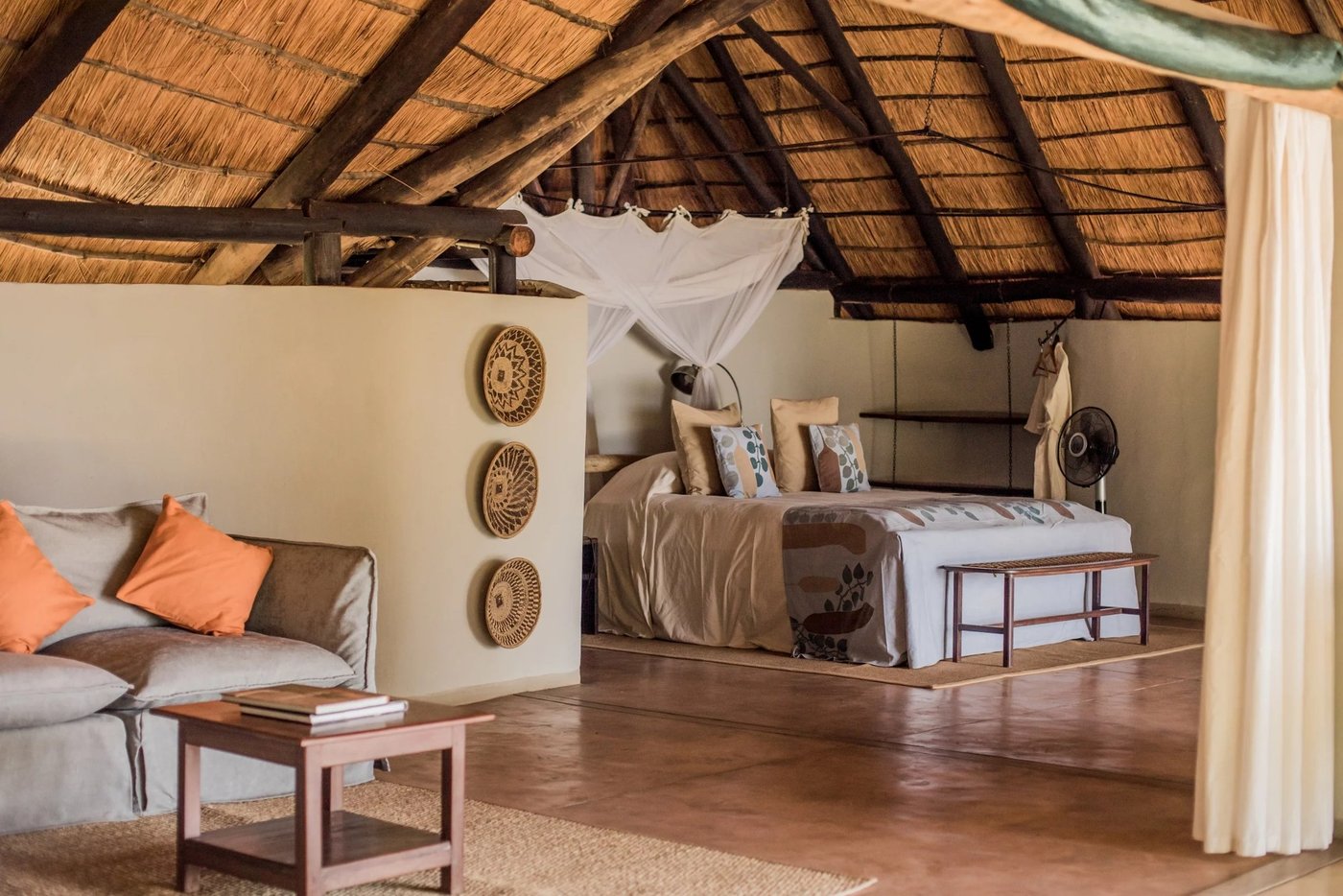 Chambre avec des coussins orange et un lit à baldaquin au Nkwali Camp