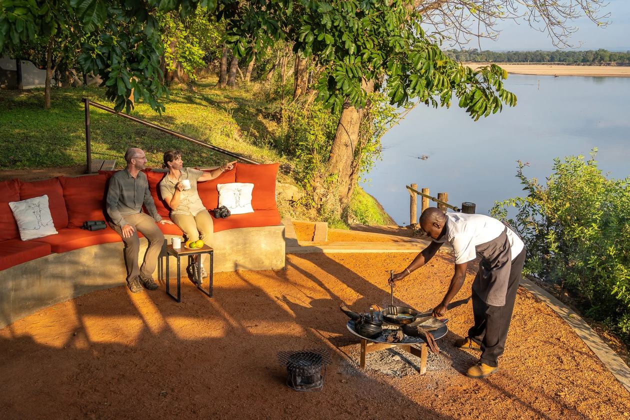 Les clients se détendent sur des canapés rouges rembourrés au bord de la rivière au coucher du soleil, Nkwali Camp