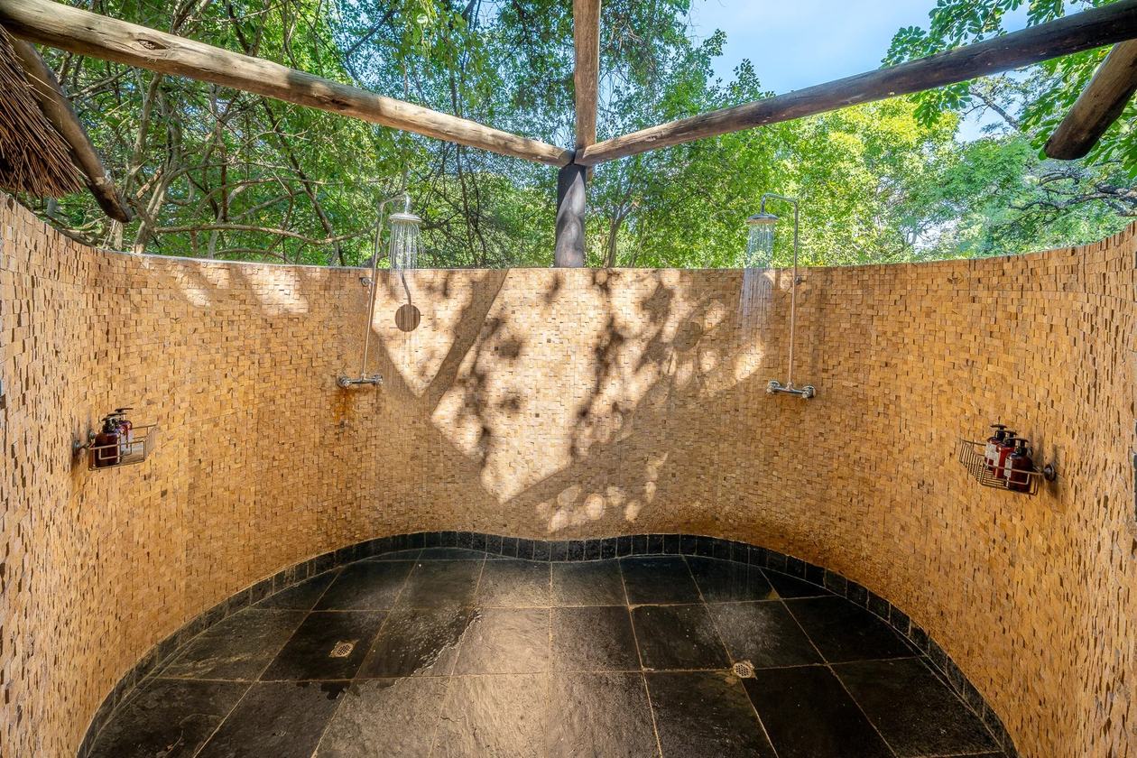 Douche en pierre à ciel ouvert sous un toit de chaume au Nkwali Camp