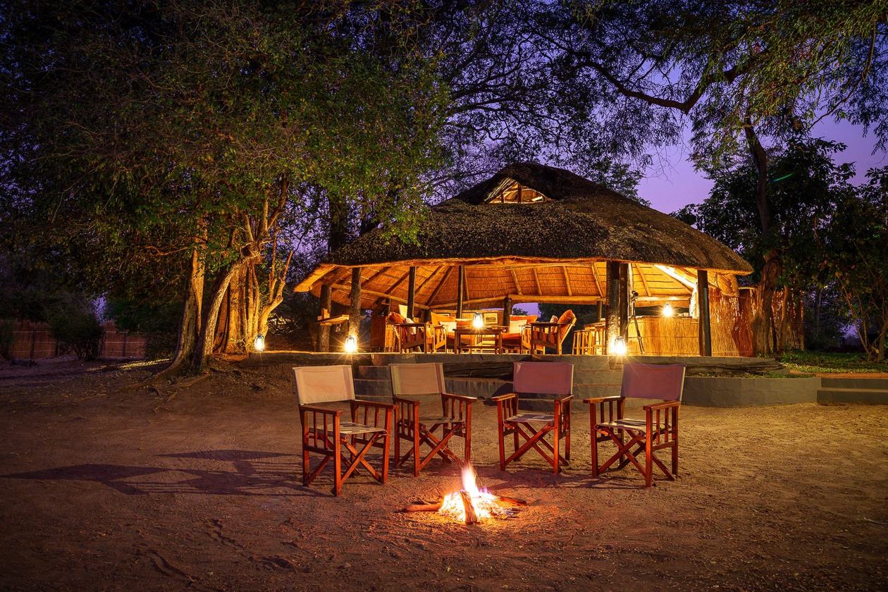Salle à manger en chaume éclairée par la lumière du feu au crépuscule, Nsefu Camp, South Luangwa
