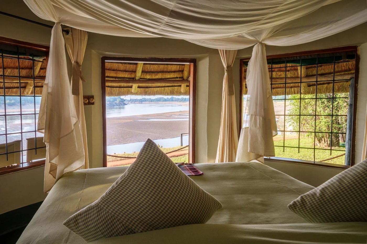 Chambre avec une fenêtre à rideaux encadrant la vue sur la rivière chez Nsefu Camp