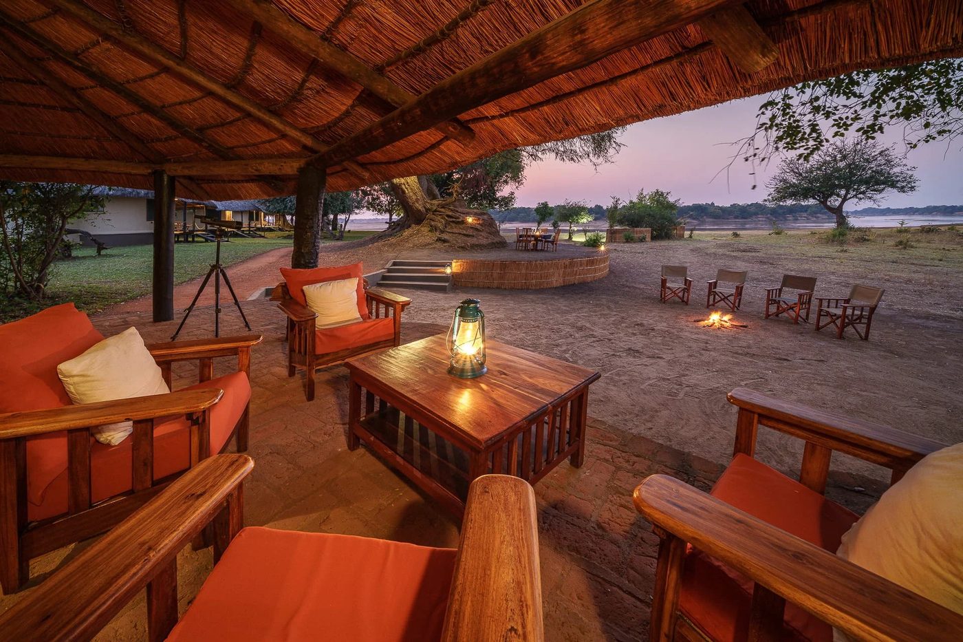 Terrasse de salon avec coussins orange et lanternes sous le chaume de Nsefu Camp