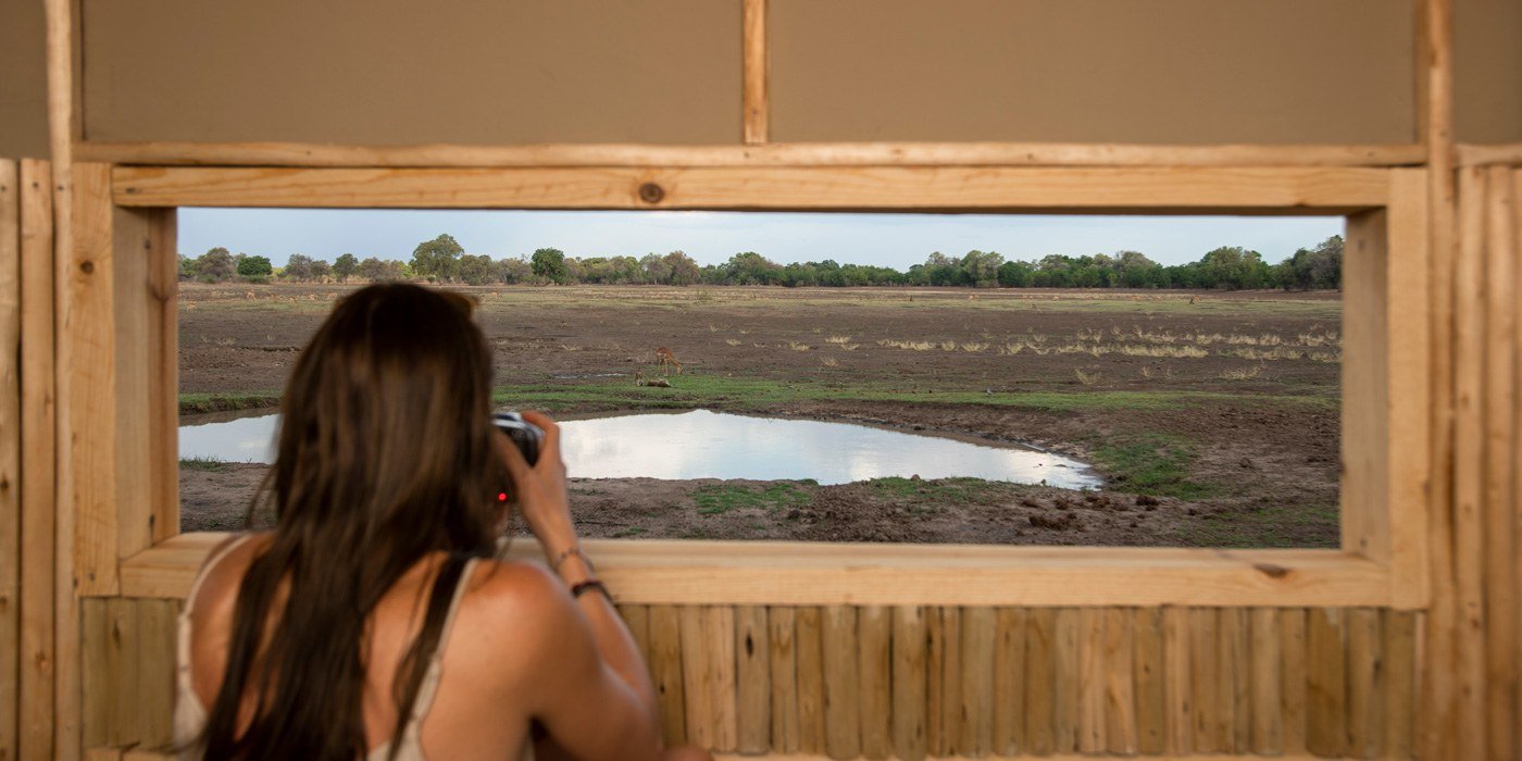 Un visiteur regardant par la fenêtre de l'affût photographique à Puku Ridge, South Luangwa