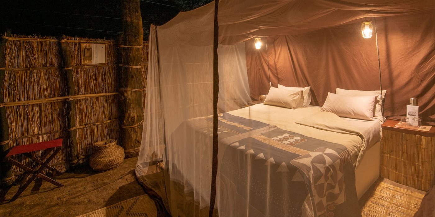 Un filet anti-moustiques drapé au lit dans un chalet éclairé par des lanternes à Tafika Camp