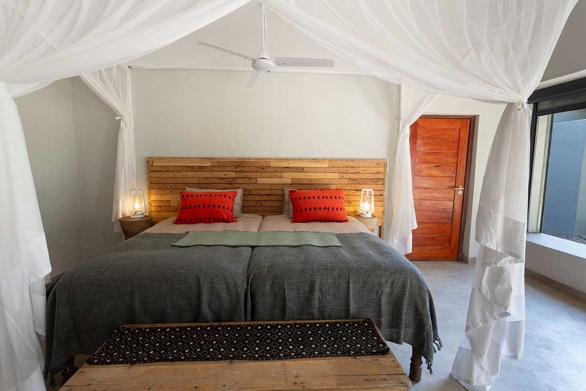 Chambre sous une moustiquaire avec des coussins rouges à Zikomo Safari Camp