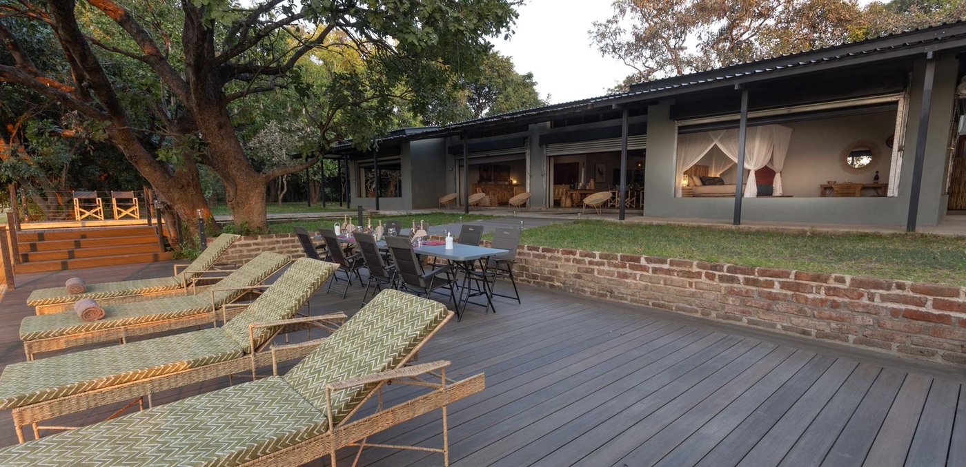 Terrasse de la piscine avec des chaises longues sous la ligne du toit en chaume à Zikomo Safari Camp