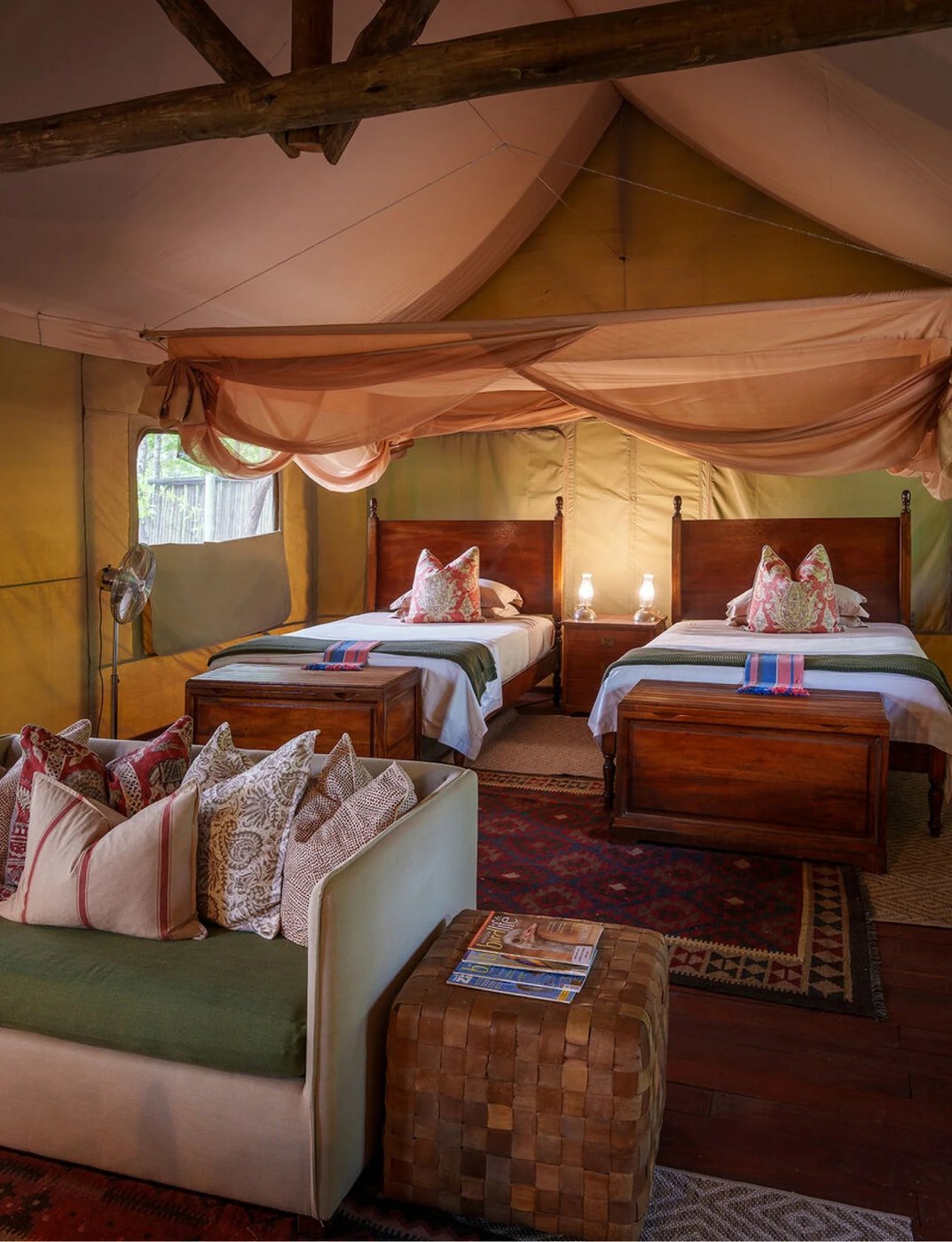 Lits jumeaux avec têtes de lit sculptées sous un dais drapé à Zungulila Bushcamp