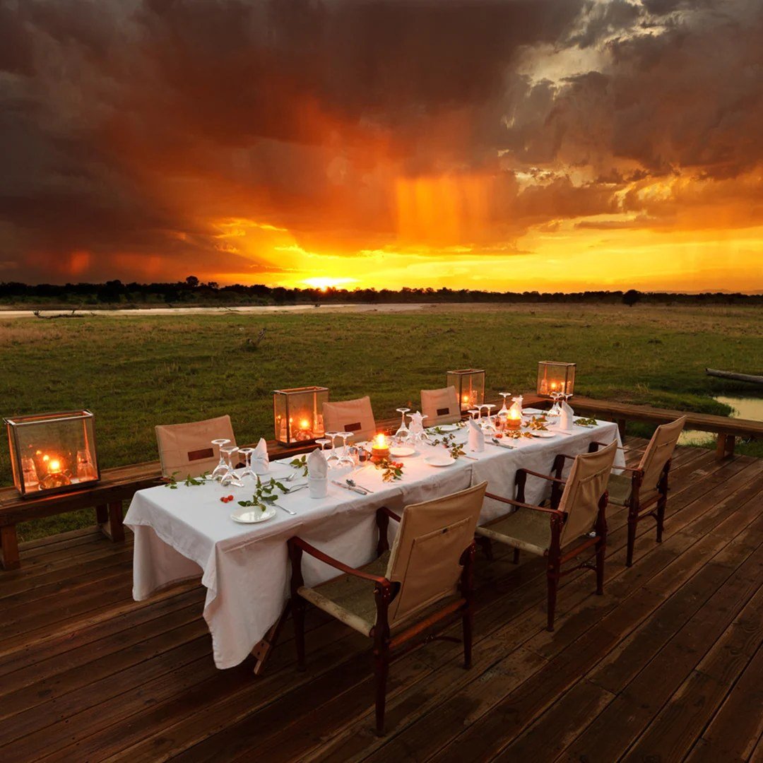 Table de dîner dressée sur la terrasse sous un coucher de soleil dramatique à Zungulila Bushcamp