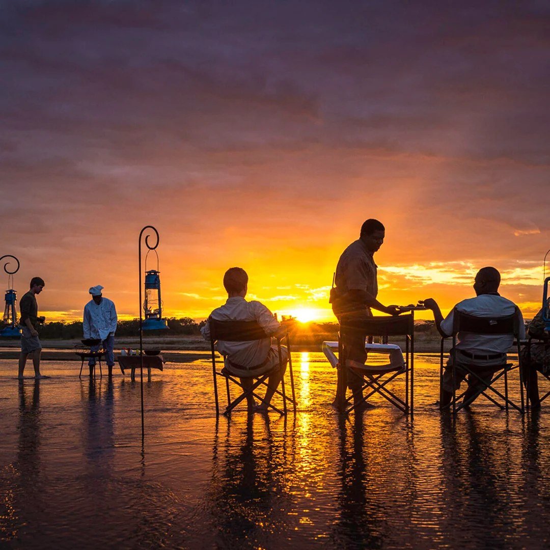 Les guides préparent les apéritifs du soir sur un pan (dépression humide) inondé alors que le soleil se couche à Zungulila Bushcamp