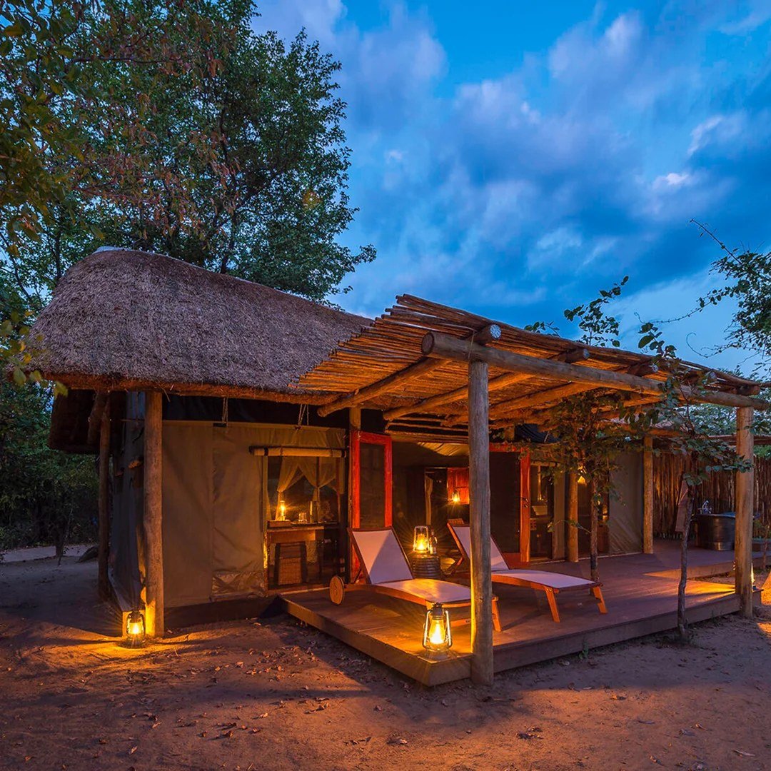Des chaises longues attendent sur une terrasse éclairée par des lanternes alors que la soirée tombe à Zungulila Bushcamp